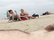 Een nudistenman ejaculeert op het strand terwijl twee vrouwen naar hem kijken
